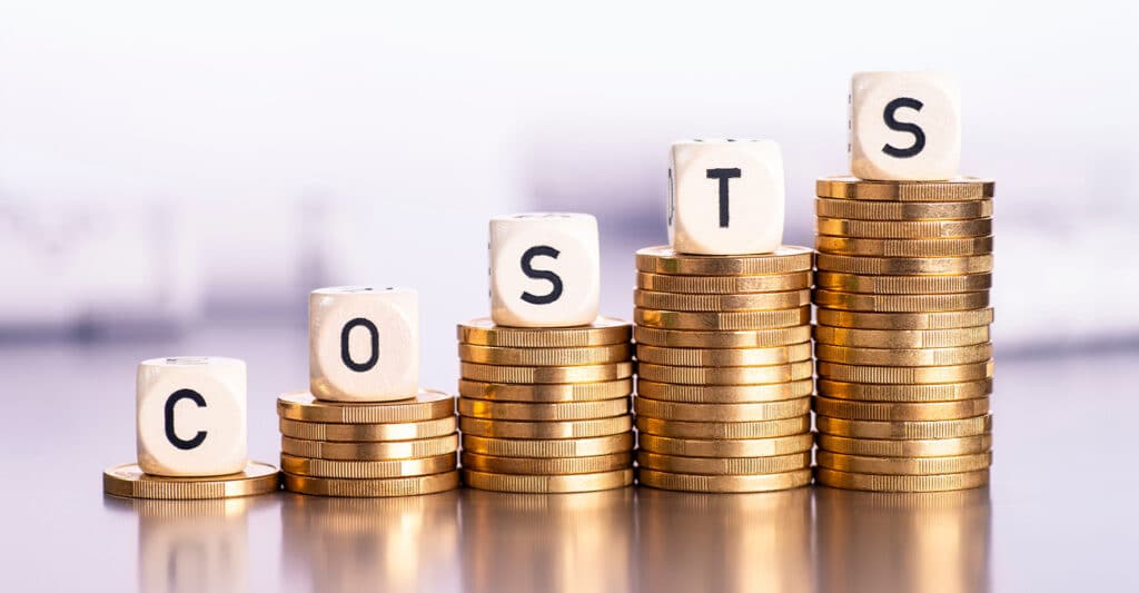 Trade Show Costs: A Complete Breakdown for Exhibitors 3 Wooden letter blocks spelling COST sit on top of stacked gold coins arranged in ascending columns. The growing stacks of coins visually represent rising costs or increasing expenses in a financial concept image.