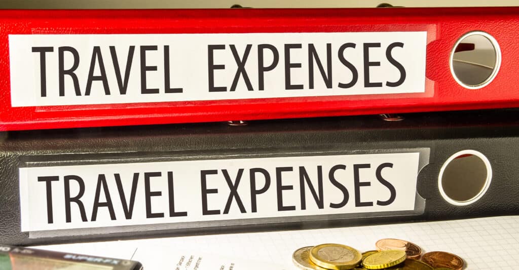 Trade Show Costs: A Complete Breakdown for Exhibitors 7 Two office binders labeled TRAVEL EXPENSES sit stacked on a desk, one red and one black, with coins and paperwork partially visible below. The labeled binders clearly organize travel expenses, highlighting record keeping and expense tracking for business or reimbursement purposes.