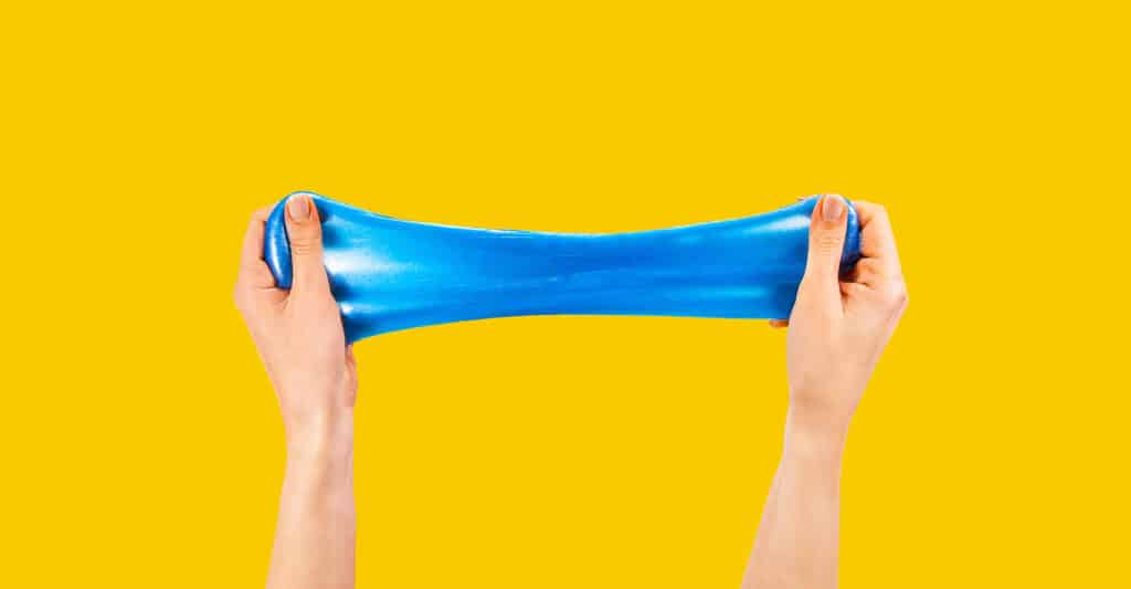 Trade Show Costs: A Complete Breakdown for Exhibitors 11 Two hands stretch a piece of bright blue slime horizontally against a solid yellow background. The smooth elastic texture and vibrant colors create a playful visual of sensory play, flexibility, and stress relief.