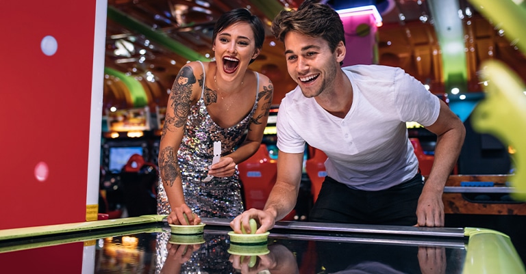 Surefire Trade Show Themes that Will Draw a Big Crowd 8 A cheerful couple playing air hockey at an arcade, laughing and enjoying the game.