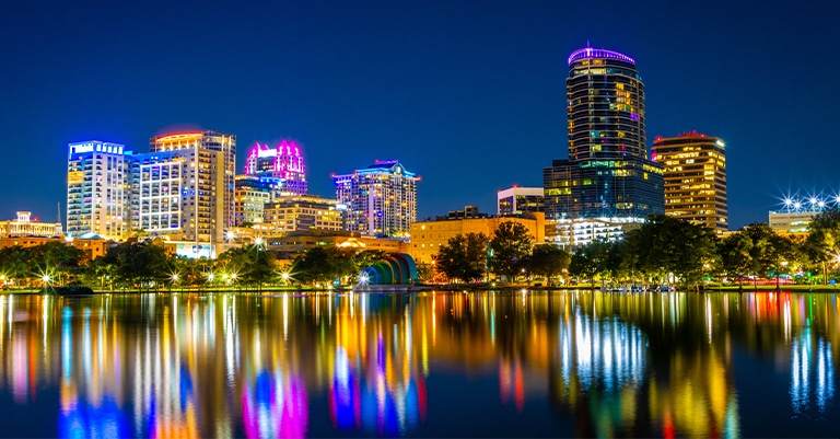 Top Trade Show Cities in the US: The Ultimate List 4 Downtown Orlando skyline at night with colorful building lights reflected in the calm waters of Lake Eola.