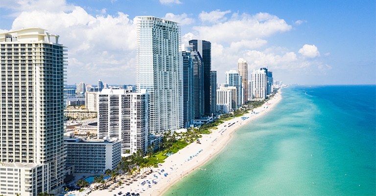 Top Trade Show Cities in the US: The Ultimate List 9 Aerial view of Miami Beach with high-rise buildings along the shoreline and turquoise ocean waters under a sunny sky.
