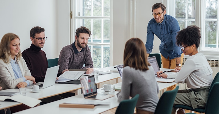 Trade Show Booth Activation: How to Make it All Work 4 A group of professionals in a modern office engaged in a team meeting with laptops and documents on the table.